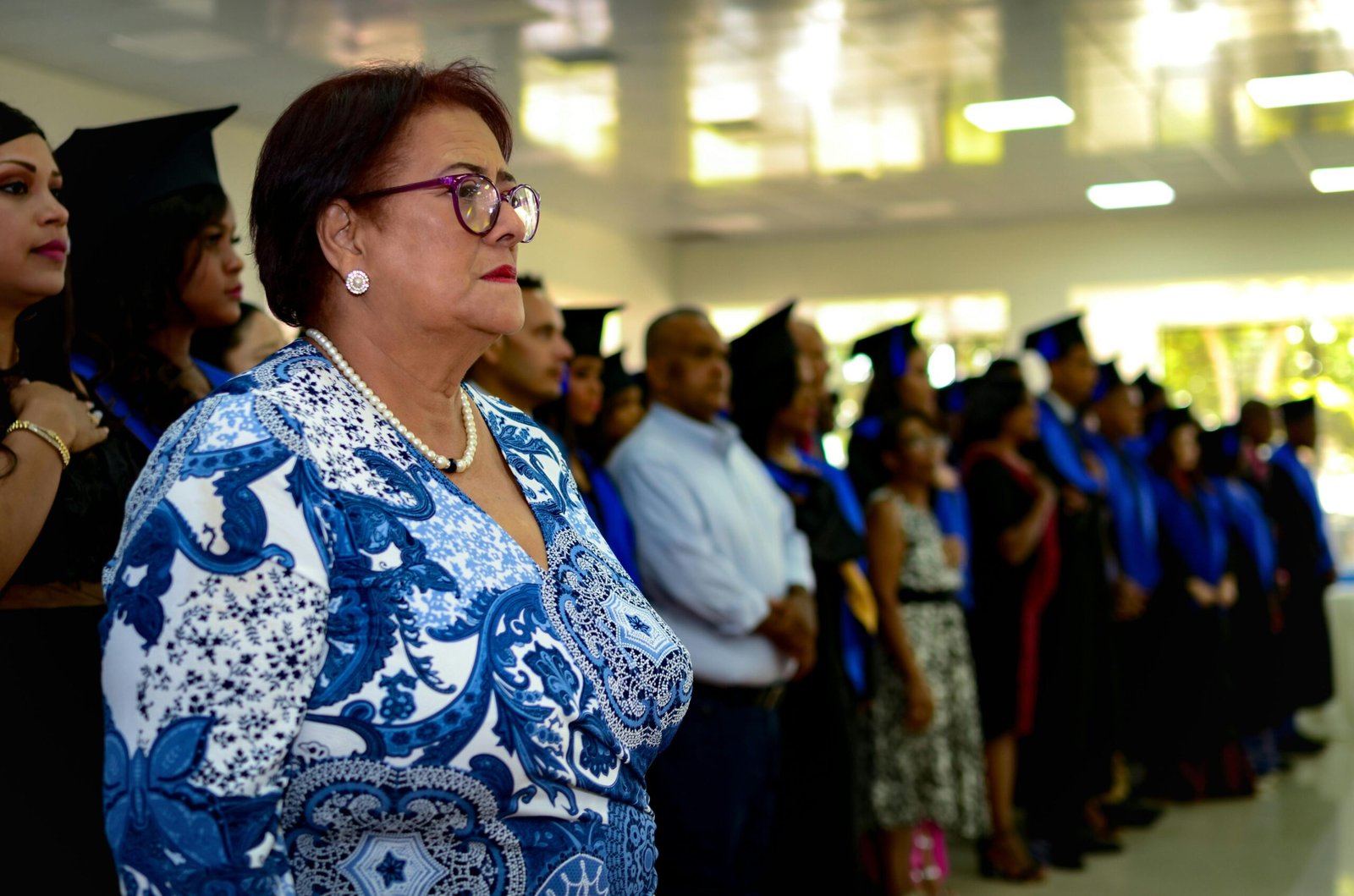 Graduation ceremony with guests and graduates in caps and gowns indoors.