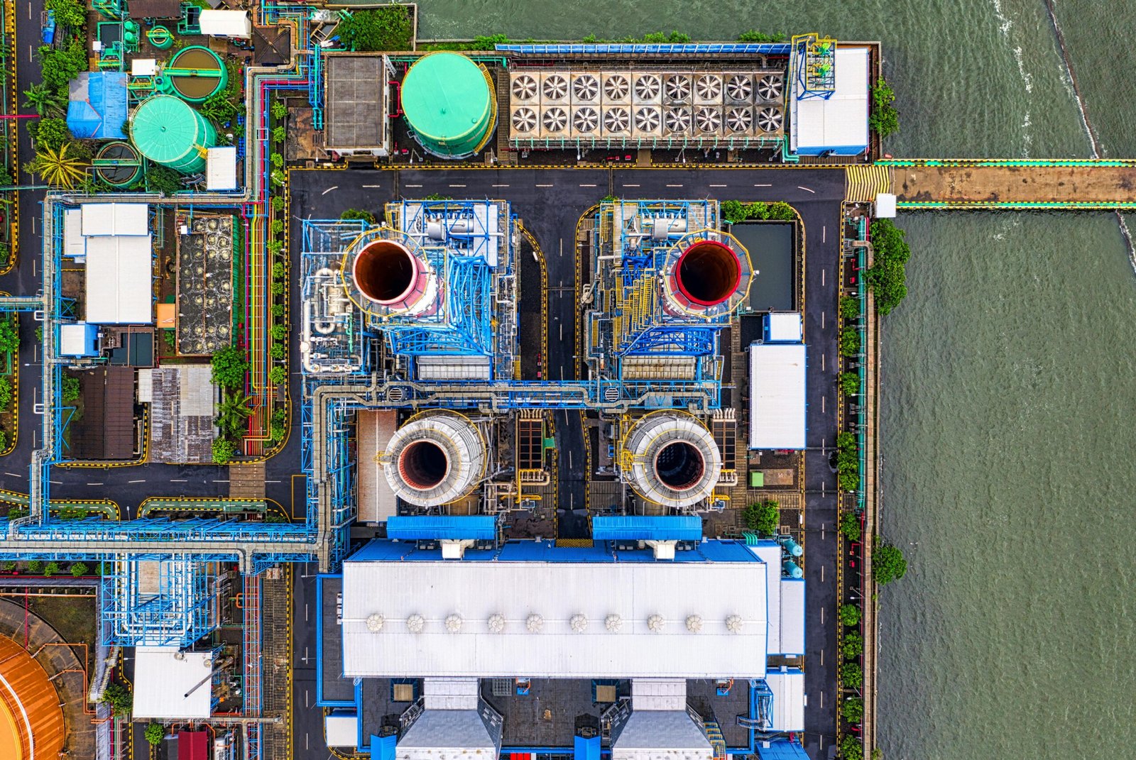 Aerial view of an industrial plant in Jakarta by the waterfront. Features colorful structures and piping.