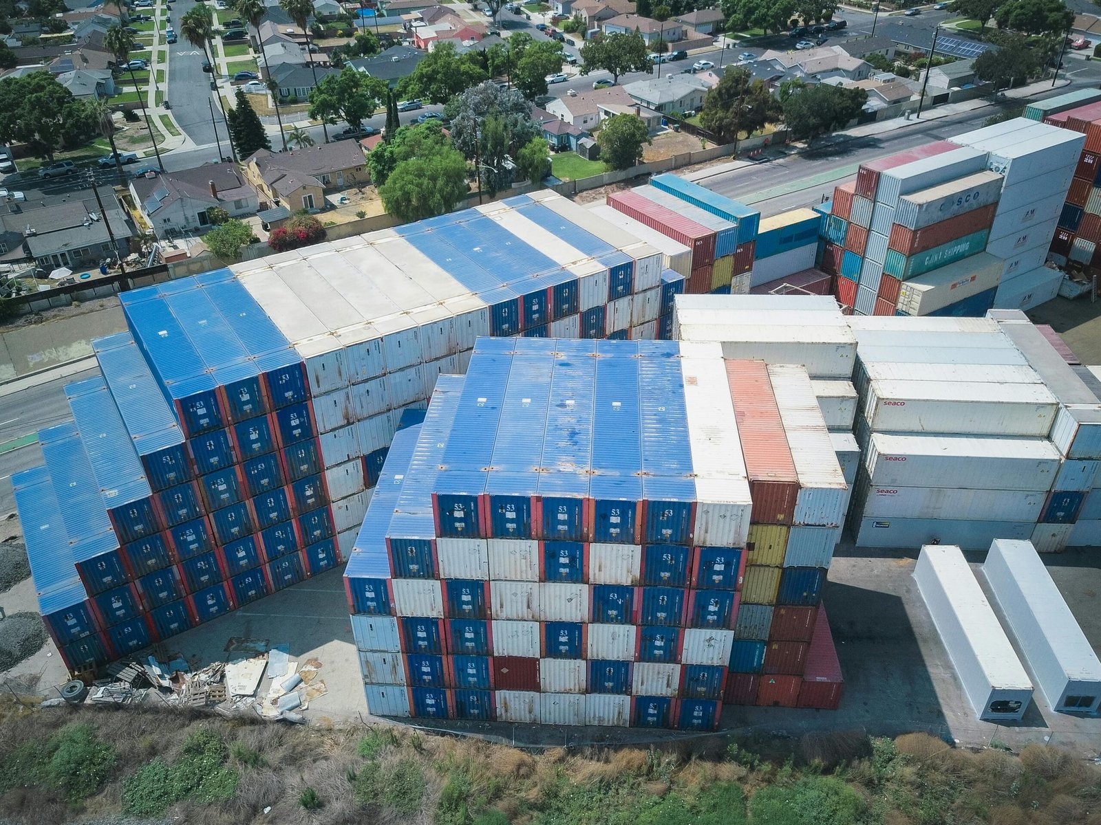 Drone shot of cargo containers stacked by residential houses, showing urban storage.