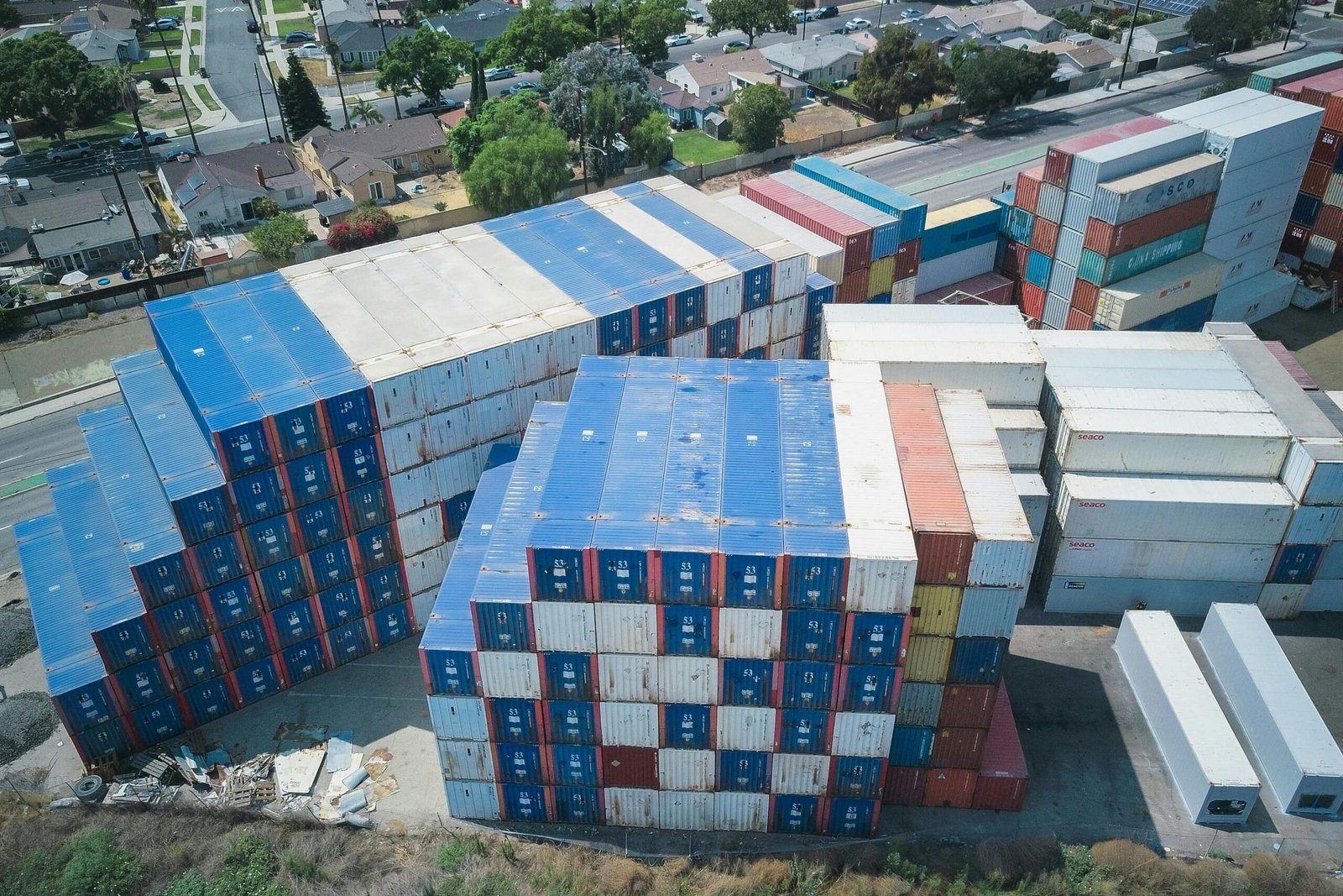pexels-photo-9716376-9716376 Drone shot of cargo containers stacked by residential houses, showing urban storage.